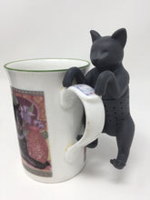 Load image into Gallery viewer, Black cat-themed tea infuser hanging on the side of a teacup