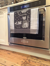 Load image into Gallery viewer, Picture of a black and white cat-themed kitchen towel hanging from an oven handle bar