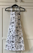 Load image into Gallery viewer, Picture of a white and black kitchen apron on a black hanger featuring black cats